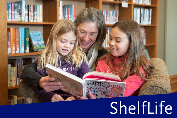 Grandmother and two grand-daughters reading together in library