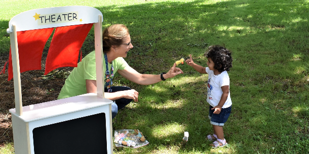 Outreach Manager Lorraine Lane smiling and playing puppets with a smiling toddler at a recent FCPL Bookmobile stop. 