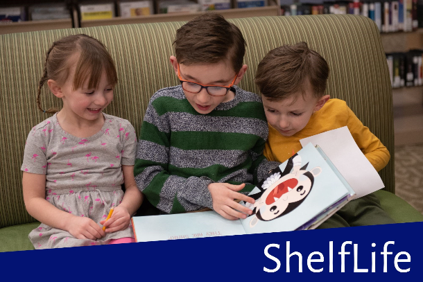 Three kids in library's children's area reading a book together
