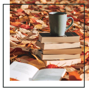 A coffee cup on top of a stack of books on a leaf-covered ground