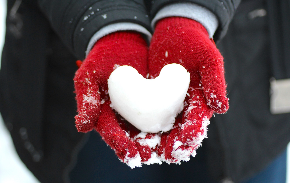 A photo of a person wearing red gloves and holding a heart made out of snow.