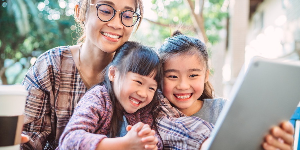Mother and two young girls smiling while looking at an electronic tablet because they are reading the latest Weekly Program Planner newsletter from FCPL featuring all the amazing library programs coming up in the week ahead. 