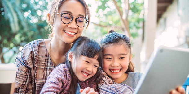 A mom and her two young daughters are reading their Weekly Program Planner newsletter. They are all smiling because they're so excited about all the fabulous programs they're going to attend next week at FCPL! 