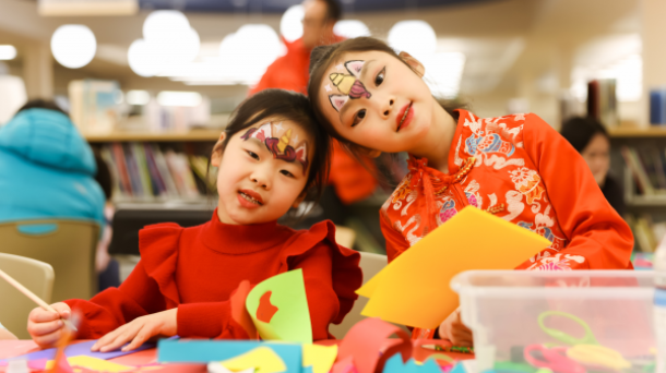 Two young Asian girls dressed in red celebrating Lunar New Year at Sharon Forks Library. 