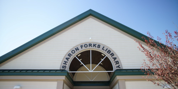 Close-up of entrance to Sharon Forks Library with blue sky above and spring tree in bloom by photographer Boon Vong. 