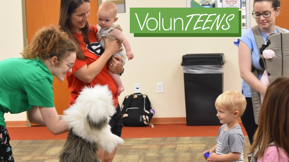 A smiling VolunTEEN entertaining a preschool child with a sheepdog puppet while smiling adults watch. Being a VolunTEEN at FCPL is so fun and rewarding!
