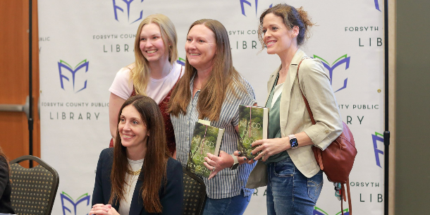 Liz Moore signing The God of the Woods books with three attendees standing behind her at Forsyth Reads Together 2026.