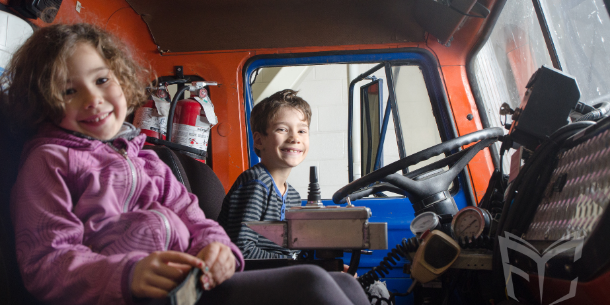 Two smiling children sitting in a firetruck. 