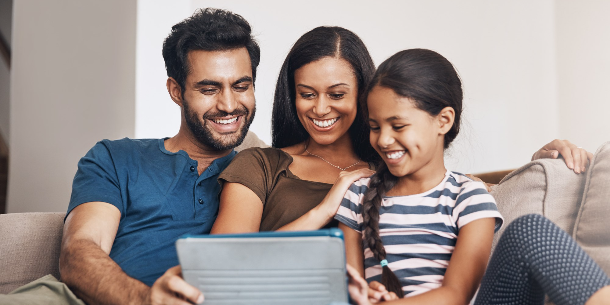 Family of three smiling people sitting on a couch and looking at a digital tablet together. 