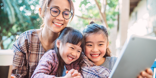 Two young girls and an adult woman smiling and interacting with content on a handheld tablet screen.