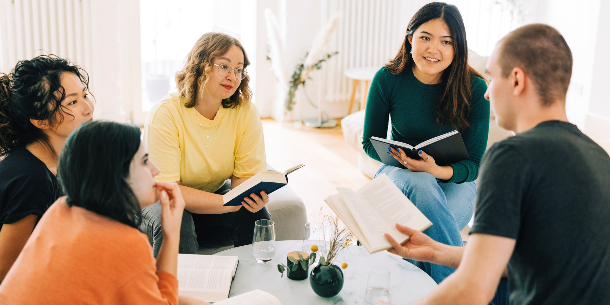 Group of five young adults discussing books around a table. 
