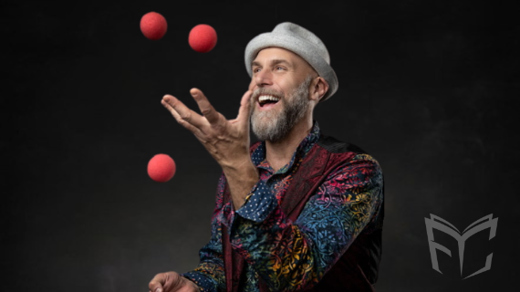 Man in front of a black background juggling three red balls. 