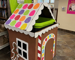Photo of a large bin decorated like a gingerbread house to collect food donations at Hartland Public Library.