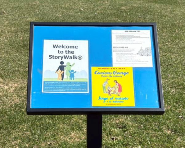 StoryWalk sign with "Curious George Visits the Library" book inside at Ralph Park. StoryWalk sign with "Curious George Visits the Library" book inside at Ralph Park.