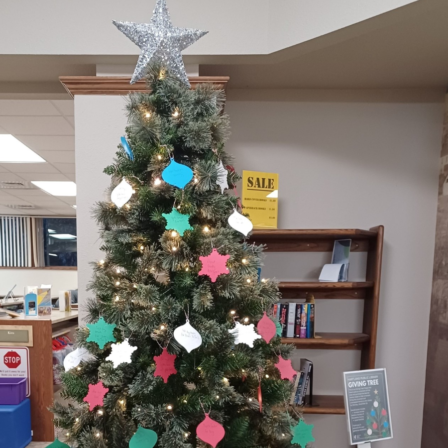 Photo of the Giving Tree decorated with colorful tags in the shape of ornaments inside the library.