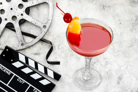 A cocktail garnished with fruit next to a film reel and a clapperboard.