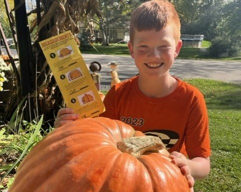 Photo of a young boy smiling at the camera with his giant pumpkin.