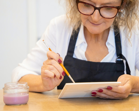 Stock photo of a woman in glasses painting on a small canvas in her hands.