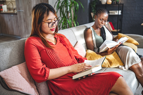 Two people reading books on a couch together.
