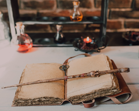 Open book on table with a wand laying across the book.