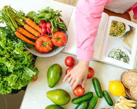 Stock photo of hands reaching towards tomatoes and other vegetables with an open cookbook near. Stock photo of hands reaching towards tomatoes and other vegetables with an open cookbook near.