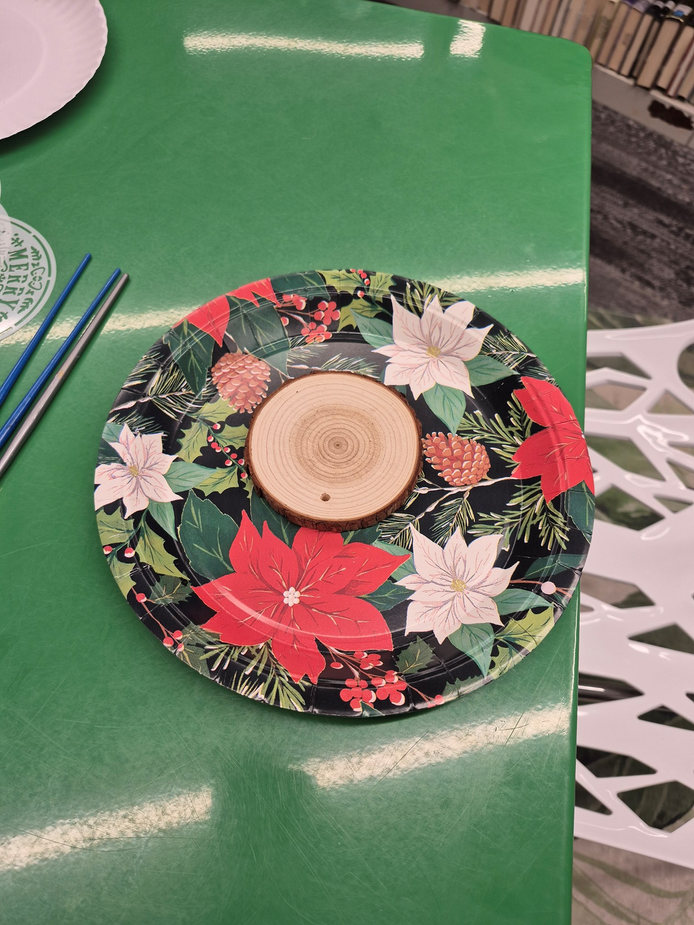A wood ornament resting on a plate on a green table in the Teen Scene.