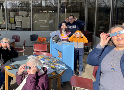 Patrons stand outside using solar eclipse glasses to look at the sun Patrons stand outside using solar eclipse glasses to look at the sun