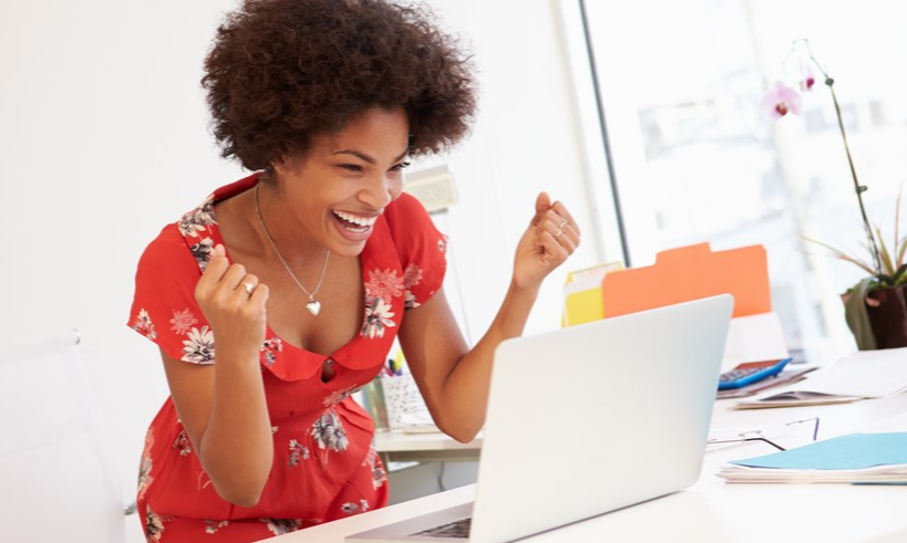 Laughing woman in a red dress standing in front of a laptop.